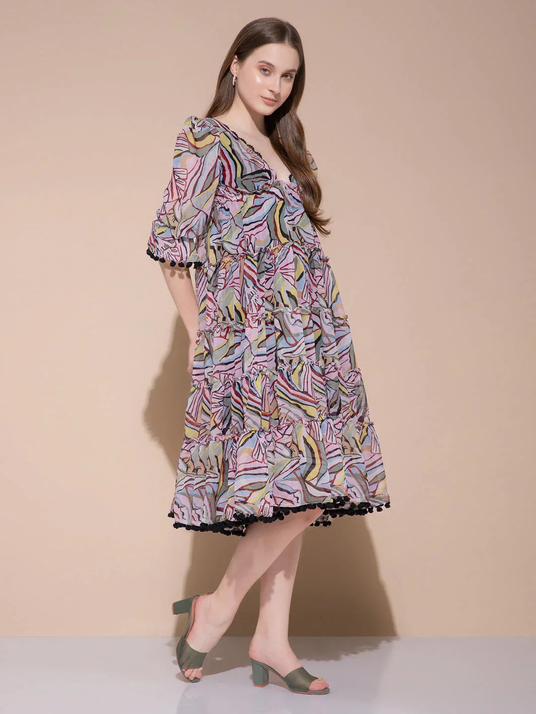 Woman wearing a colorful abstract print midi dress with puff sleeves and black pom-pom trim