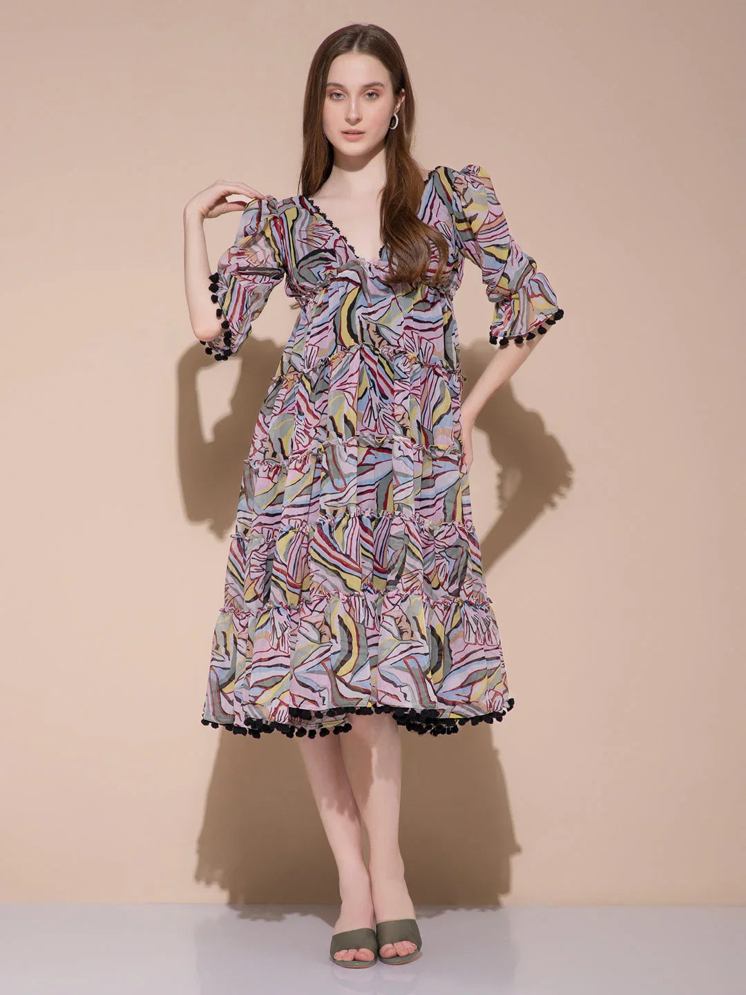 Woman wearing a colorful abstract print midi dress with ruffled sleeves and black pom-pom trim