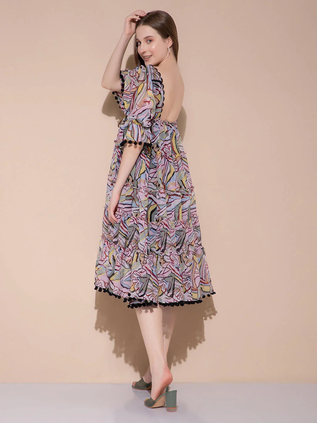 Woman wearing colorful abstract print midi dress with puff sleeves and open back, standing on light gray floor