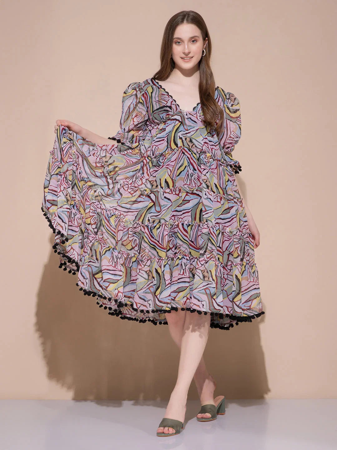 Woman wearing colorful abstract print midi dress with puff sleeves and black pom-pom trim posing on beige background
