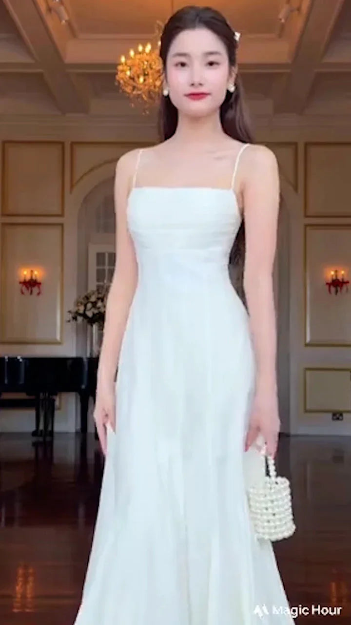 Woman wearing white flared maxi dress holding pearl handbag in elegant room with chandelier