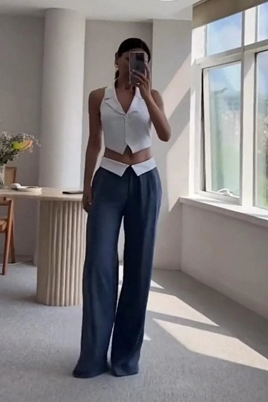 Woman in white sleeveless cropped vest and wide-leg blue pants taking mirror selfie in bright room