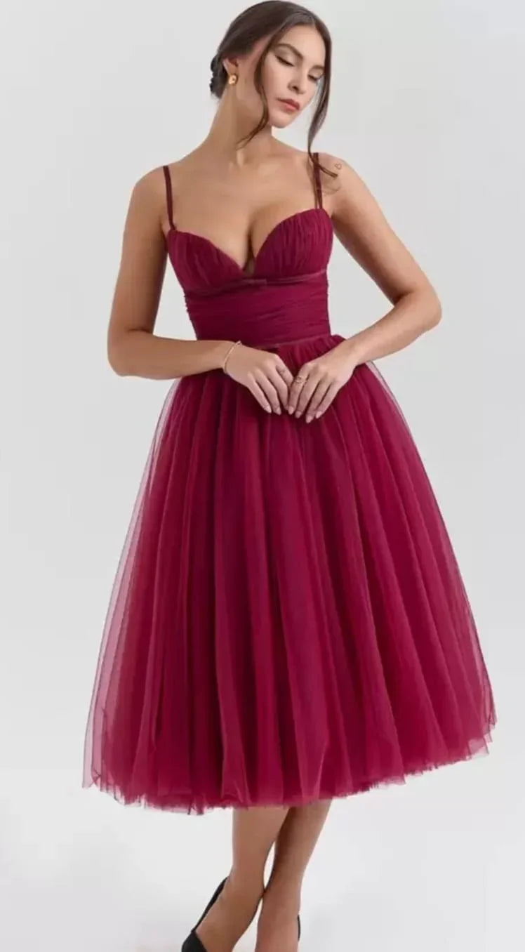 Woman in elegant burgundy tulle midi dress with spaghetti straps posing against gray background