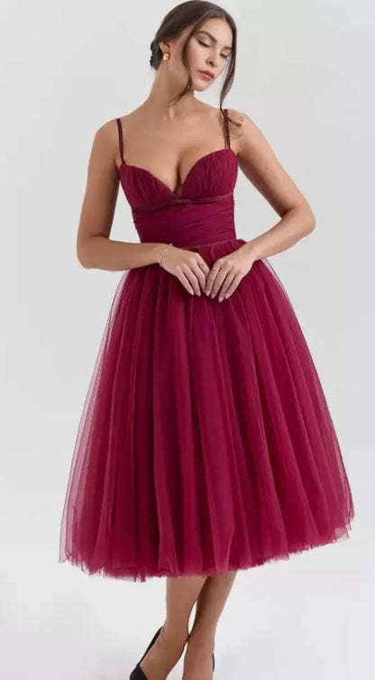 Woman in elegant burgundy tulle midi dress with spaghetti straps posing against gray background