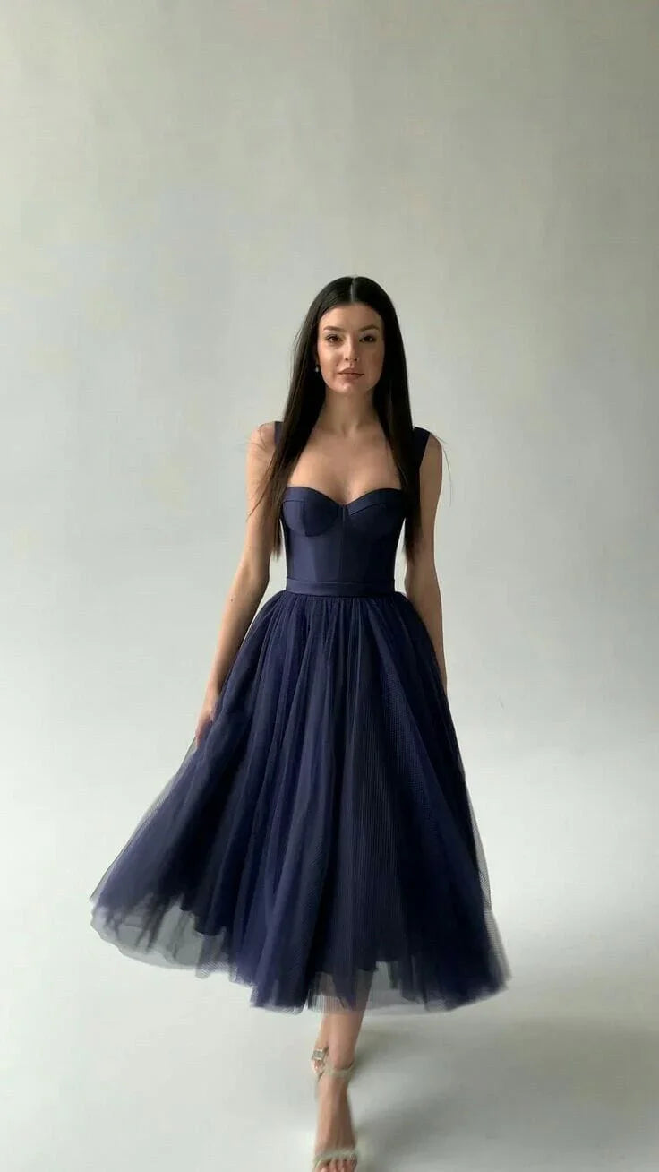 Woman in elegant navy blue tulle midi dress with fitted bodice and strapped heels against plain background