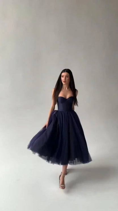 Woman in a strapless navy blue tulle midi dress with a fitted bodice walking in a studio