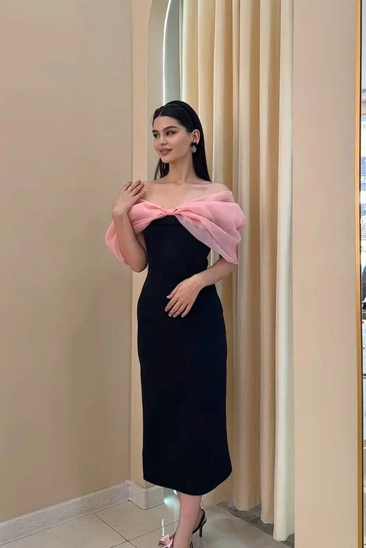 Woman wearing elegant black off-shoulder midi dress with pink chiffon bow detail indoors